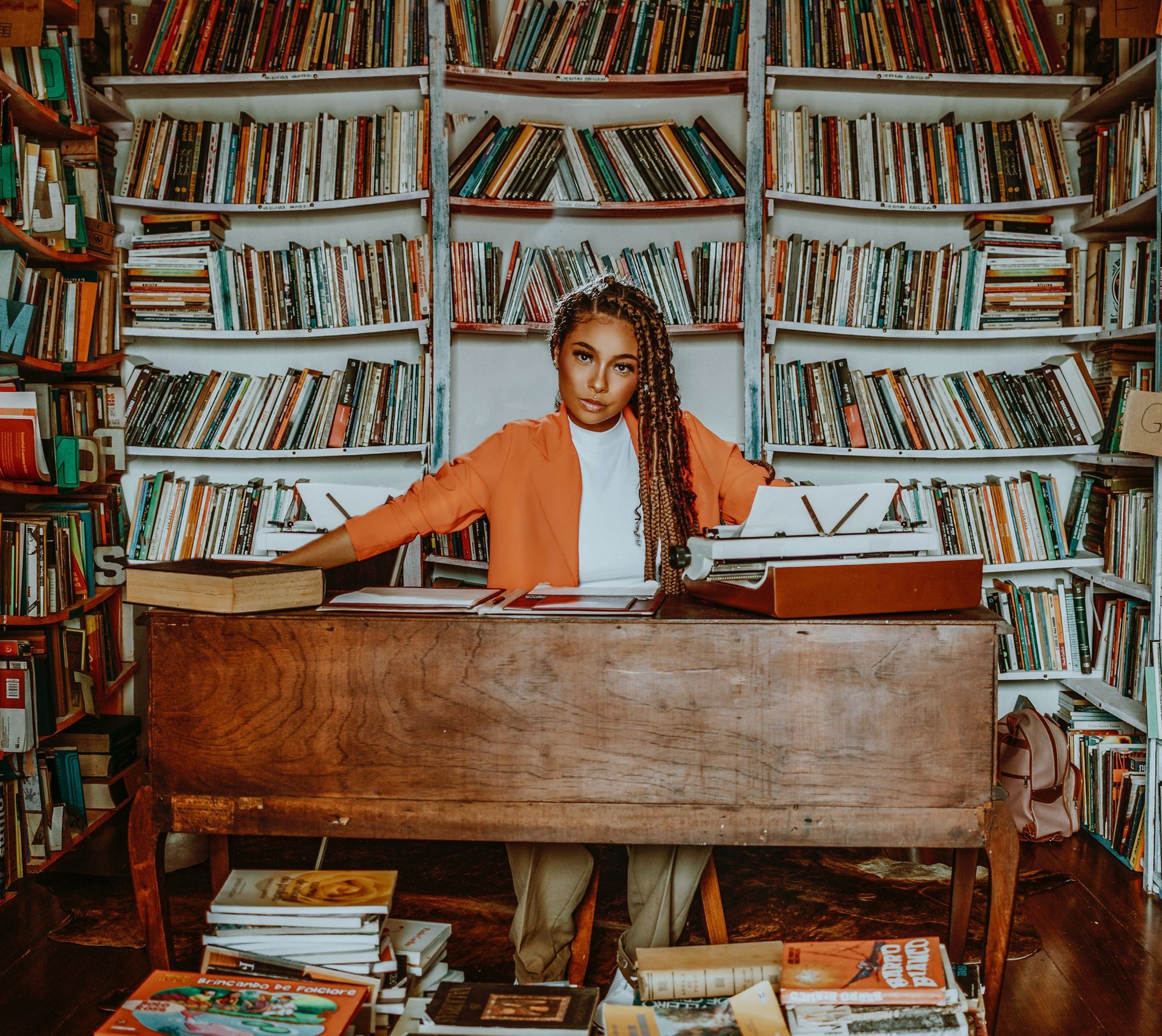 Black woman sitting at desk surrounded by shelves of books.